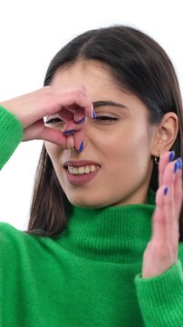 Displeased Caucasian young adult woman covering nose, reacting on bad, nasty and unpleasant smell on white background. Vertical video.