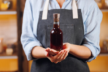 Craft master in apron holds bottle with fresh oil from black cumin
