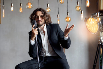 Portrait of handsome attractive singer in classic suit on grey background. Happy man singing pop...