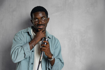 Portrait of handsome attractive african american singer on grey background. Man singing hit with open mouth in retro microphone.