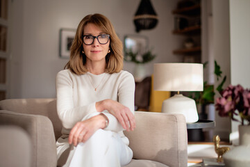 Portrait of a mature woman wearing white sweater and pants and sitting in her modern home