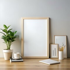 A clean and minimalist desk mockup with a large. blank picture frame. a plant. a coffee cup. a notebook. and pencils in a vase.