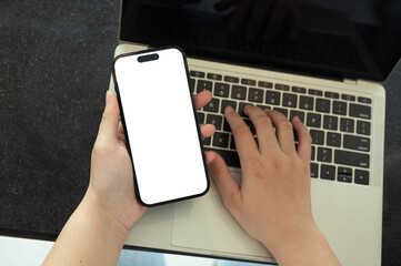 Close up image of woman holding smartphone with blank screen and using laptop