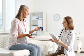 Obraz premium Smiling healthcare worker with tablet consulting senior patient in hospital