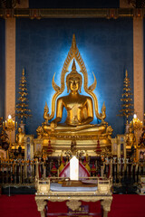 Obraz premium Thailand, August 11, 2024, Wat Benchamabophit Dusitwanaram, Golden Buddha statue in a serene temple setting with blue backdrop and ornate decorations during daylight hours