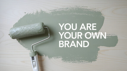 Paint roller with green paint on a wooden surface with the motivational text "You Are Your Own Brand." The image symbolizes personal branding, creativity, and self-expression