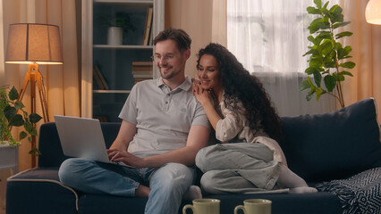 Multiracial couple shopping computer together choose e-commerce buy goods using laptop discuss at...