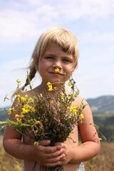 Smiling little girl with bouquet of wildflowers at field