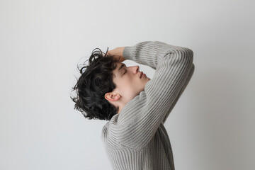 Fototapeta premium A man holding under his armpit, his sweater is grey in color with a white background, his arm is raised up to the top of his head