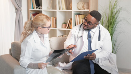 Diagnosis discussion. Healthcare teamwork. Professional medicine. Man doctor consulting woman physician on x ray illness clinic report on couch at hospital.