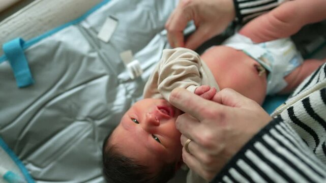 Newborn baby being gently dressed by caregiver on a soft changing mat. infant looks up calmly as the hands of the caregiver adjust the clothing with care and tenderness