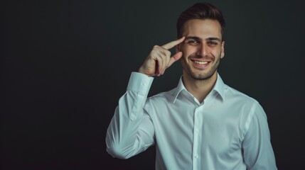 Fototapeta premium Young man pointing to his temple with a confident smile, dressed in a white shirt against a dark green background.
