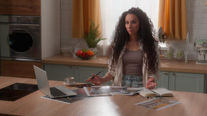 Tired stressed Hispanic woman Arabian girl Latina female lady homeowner householder at home kitchen with laptop looking on pictures photos room design templates designer renovation house interior