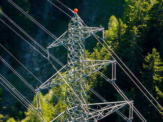 Aerial view of power line pylon in alpine forest in Switzerland. Electric current distribution with power grid.