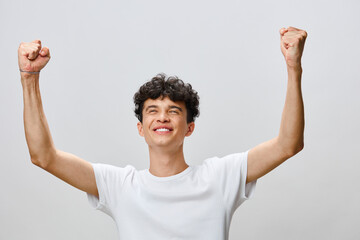 Happy young man celebrating success with raised arms and a joyful expression, wearing a white t...