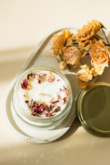 Handmade candle from paraffin and soy wax in glass with wooden wick and dry herbal isolated on pastel beige background. Flat lay, top view, copy space