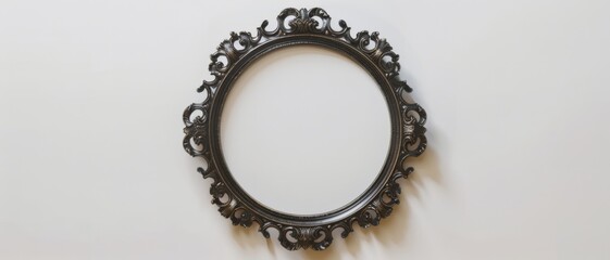 An ornate empty round picture frame with intricate details hangs on a plain white wall, waiting to be filled with memories.