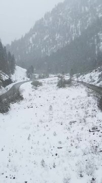 winter mountain valley cars driving forward aerial snow covered flocks falling white forest trees street road stream water