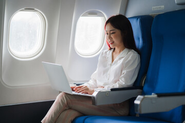 Businesswoman on Flight:  A young woman in a white blouse and pink pants is seated on an airplane, smiling as she works on her laptop. The photo captures the sense of calm and productivity that many b