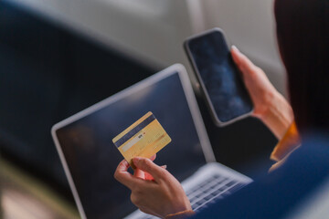 Online Shopping Convenience: A close-up image of a person's hands holding a credit card and smartphone, with a laptop in the background, capturing the ease and accessibility of online shopping.  