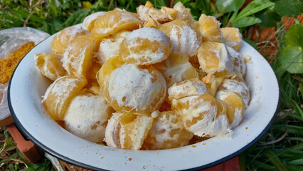 Peeled tangerines in a white plate on the grass.