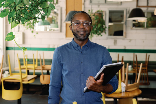Portrait of smiling black owner looking at camera in blurred cafe