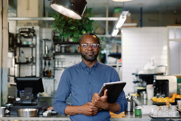 Smiling adult black entrepreneur with laptop and papers in cafe