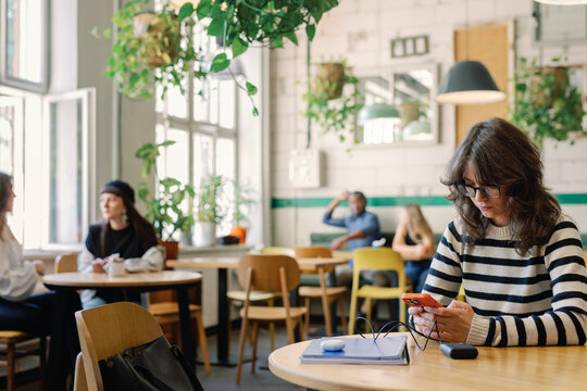 Young woman using mobile phone at table in cafe with many visitors