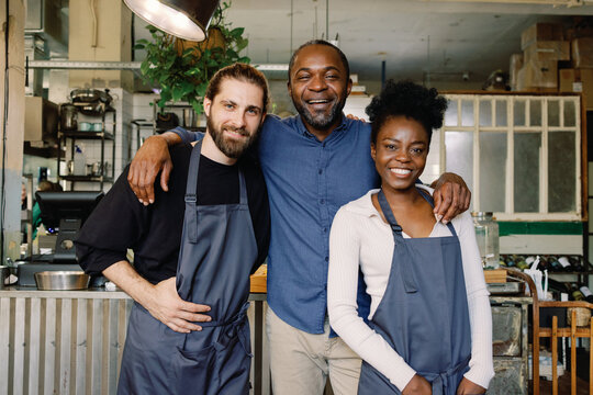 Pleased multiethnic cafe team of owner, waiter and waitress hugging