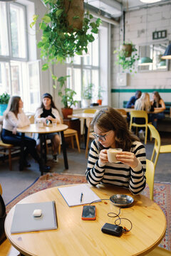 Young female student drinking coffee and looking at notebook in cafe