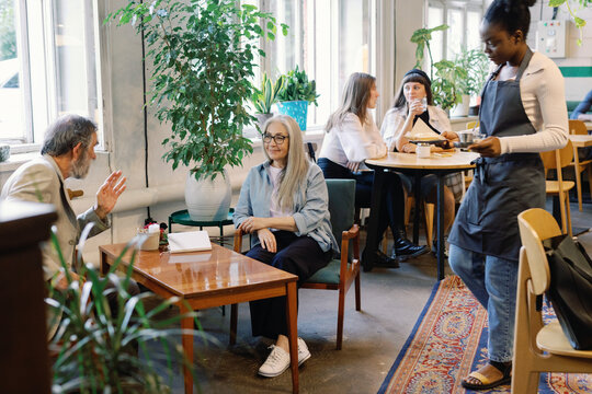 Waitress carrying coffee and cake to senior couple talking in cafe