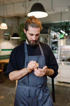 Young male bearded waiter writing order from unknown person in cafe