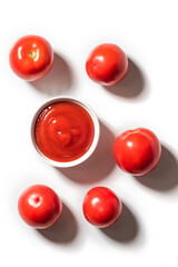 Fototapeta premium Ripe tomatoes and bowl of ketchup on white background, top view