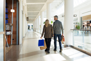 Back view of adult couple with shopping bags walking at mall
