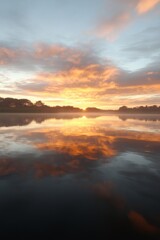 Fototapeta premium Mirror reflection of a sunset on a lake, vibrant colors and clouds, tranquil atmosphere