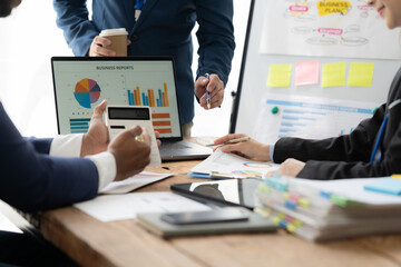Data Driven Decisions: A diverse team of business professionals collaborates around a table, analyzing data on a computer screen and whiteboards, highlighting the importance of informed decision-makin