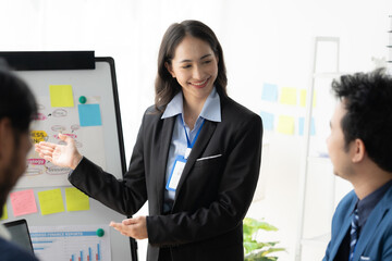 Confident Leadership: A diverse team collaborates in a modern office setting. The female leader, dressed in a professional suit, presents ideas on a whiteboard, engaging with her colleagues. The scene