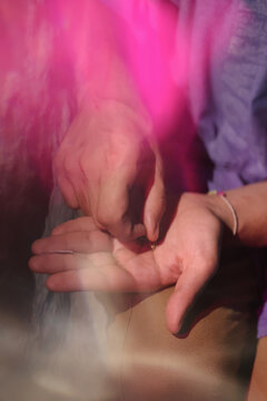 Two hands prepping marijuana for rolling and pink light effect