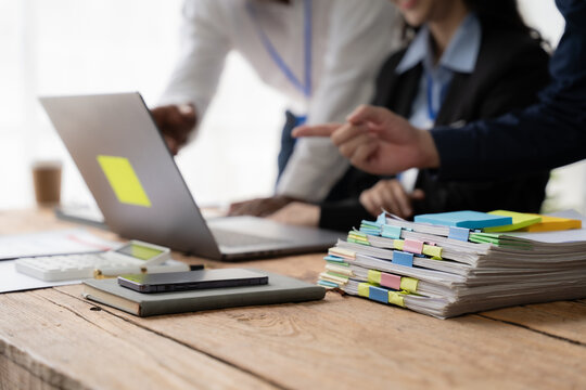 Collaborative Brainstorming Session: A diverse team huddles around a laptop, strategizing amidst a flurry of sticky notes and paperwork.