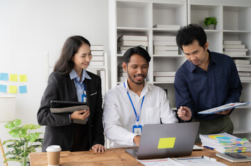 Collaborative Teamwork: A diverse team of business professionals engaged in a productive discussion, reviewing data on a laptop in a modern office setting. The image exudes a sense of collaboration, t