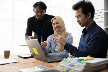 Focused Collaboration: A diverse team leans in, collaborating intently on a project around a laptop, highlighting teamwork and cultural diversity in a modern office setting. 