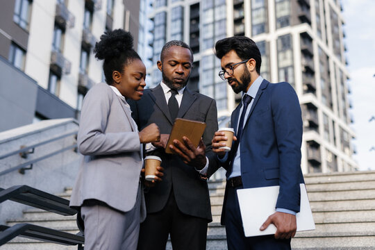 Company boss showing something on tablet to employees on stairs
