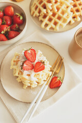 Belgian waffles with strawberries and powdered sugar on white table. Summer food concept. Soft focus