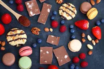 Macarons, chocolate, cookies, berries and various nuts on dark blue background. Selective focus.