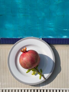 A Single Pomegranate on a White Plate by the Pool