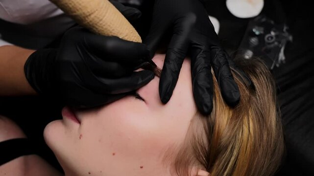 Relaxed girl is on permanent makeup procedure master is doing eyebrow tattooing. Permanent eyebrow makeup, performing eyebrow tattoo PMU