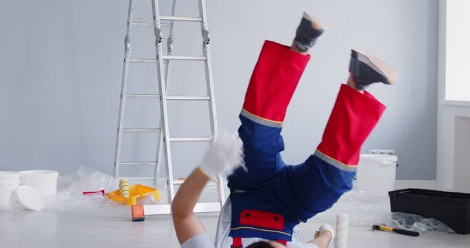 Young male painter in uniform fallen dawn from ladder while painting a wall indoors. Injured man worker after accident on workplace. Injury, insurance and safety concept. 4k video.