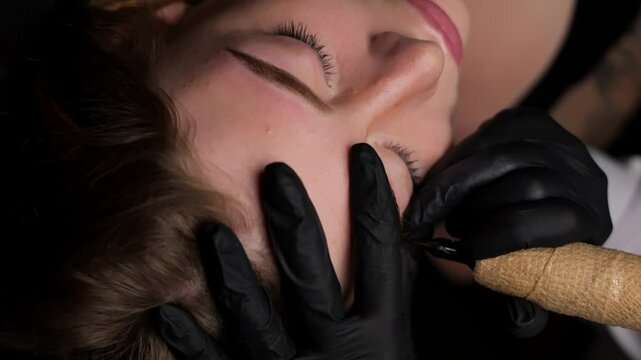 A girl with her eyes closed is lying down and she is having her eyebrows tattooed. Permanent eyebrow makeup, performing eyebrow tattoo PMU
