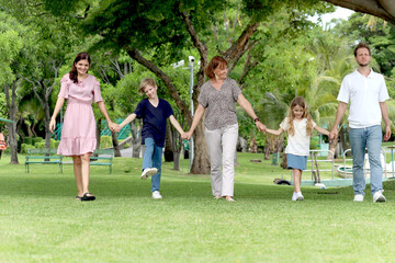 Happy cheerful family hold hands, walk in line together outside. Father, mother, daughter girl, son boy and elderly grandma take a walk in summer garden. Joyful kid, parents and senior at green park.