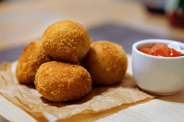 Homemade crocket from potato with filling sausages on wooden board with ketchup sauce. Side view. Close up.